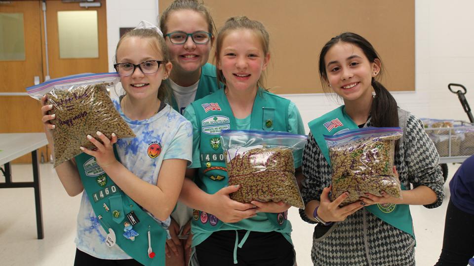 Four young scouts holding bags of pet food
