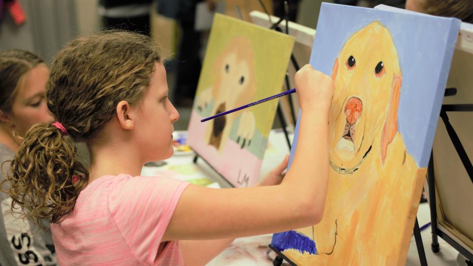 Girl in pink shirt paints yellow dog