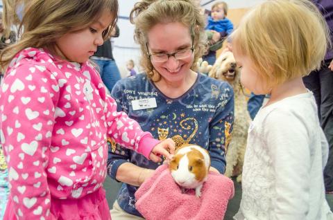 Two children and adult woman petting guinea pig 